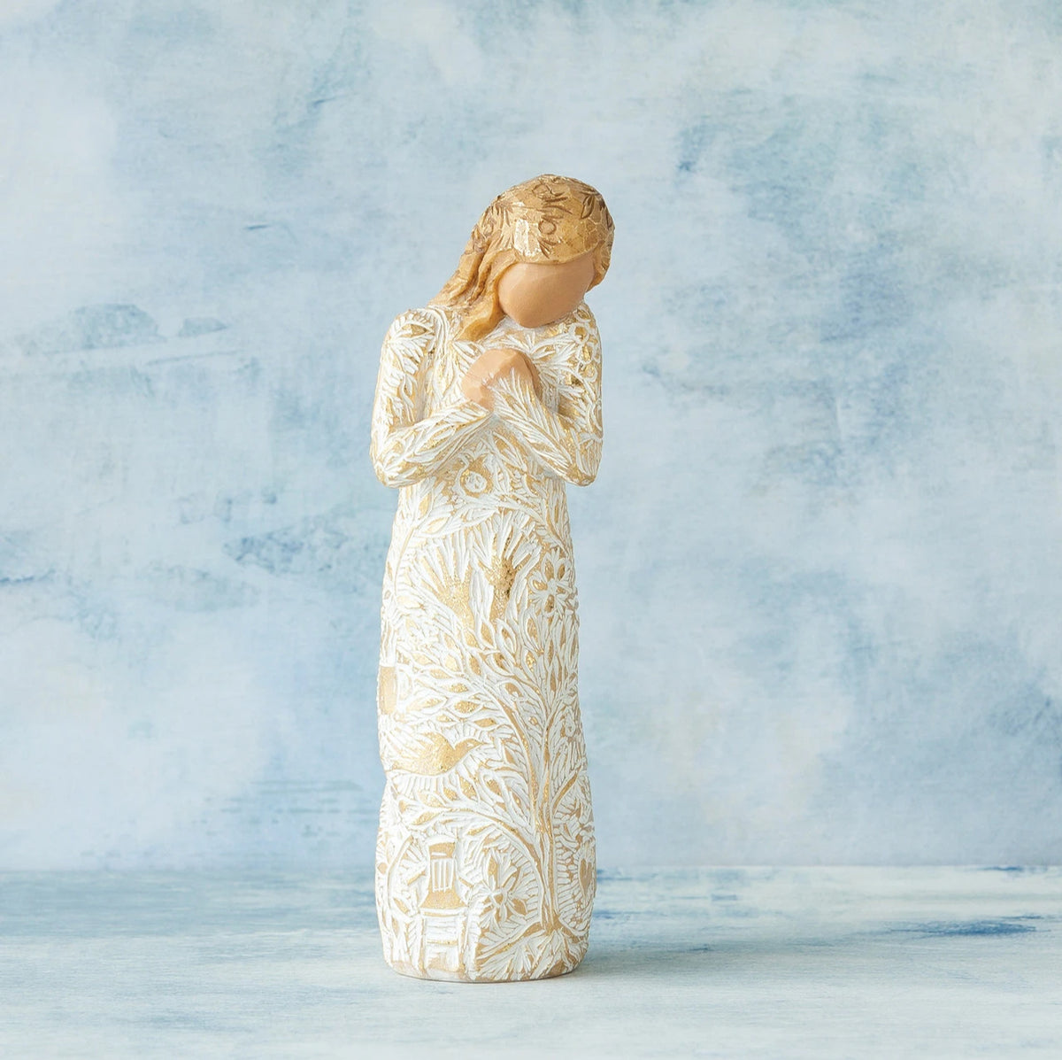 Willow Tree Tapestry, 5”h hand-painted standing resin figure, in cream dress, hands crossed at chest, entire figure carved with symbols of nature with gold-leaf, in front of blue painting