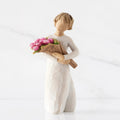 Front view of standing figure in cream dress holding bouquet of pink tulips