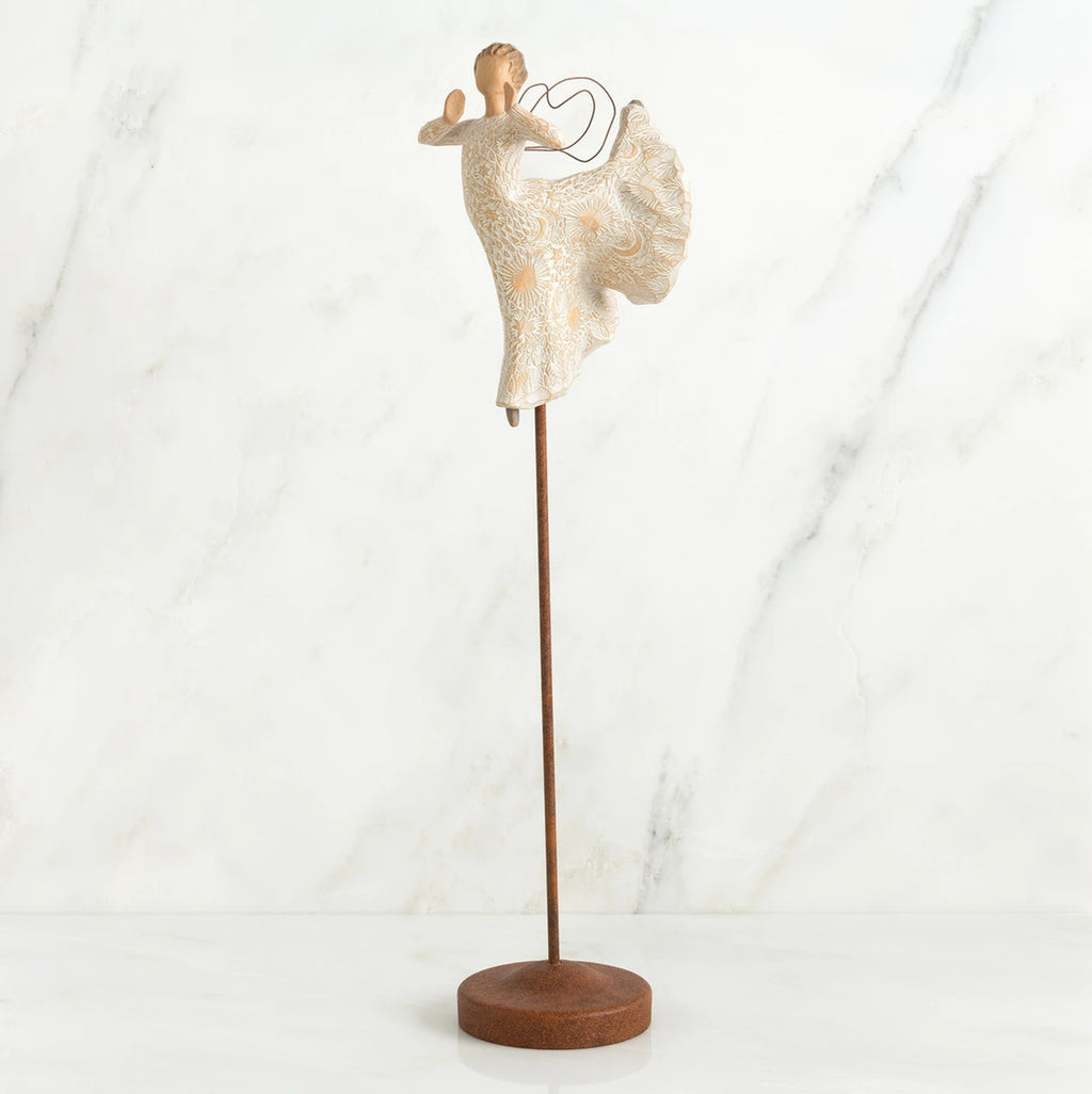 Far shot of angel figurine dressed in white dress dancing with arms and legs out - she is on a brown wooden stand