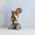 Willow Tree Kindness (boy), 3" hand-painted resin figure in neutral clothes, darker skin and hair, kneeling and holding black dog, in front of pale blue painting