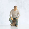 Front view, adult male figure in light gray shirt and blue jeans, seated on gray rock