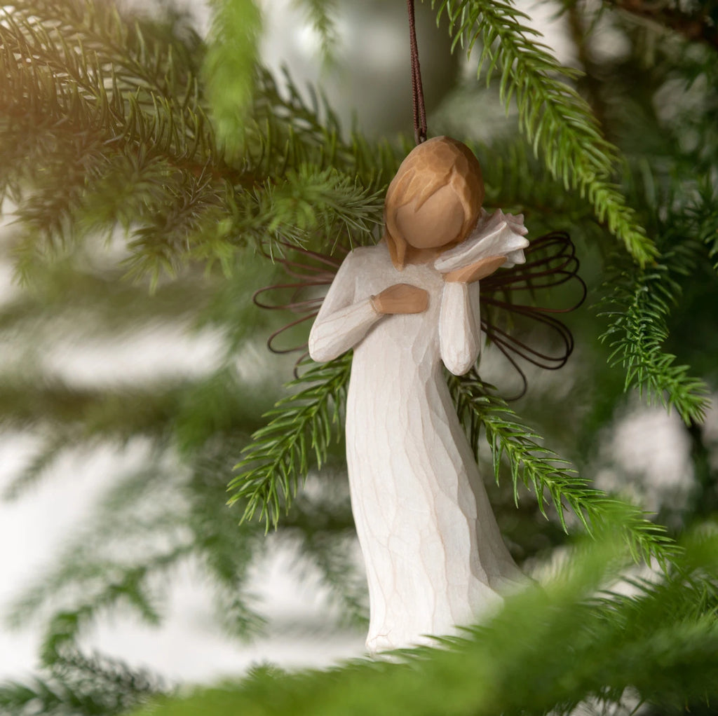 Willow Tree Thinking of You Ornament, 4.5”h hand-painted resin angel figure in cream dress with wire wings, holding pink conch shell to ear, brown elastic cord, hanging on Christmas tree