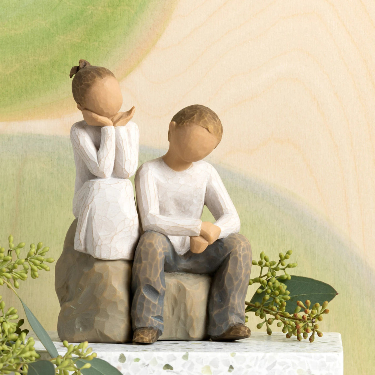 Willow Tree Brother and Sister, 5.5”h hand-painted resin figure of boy and girl, seated together on gray rock, both in neutral clothing, in front of pale green painting