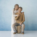 Man figurine sitting on rock wearing brown shirt and blue jeans with woman figurine in white dress with arms wrapped around him - blue background