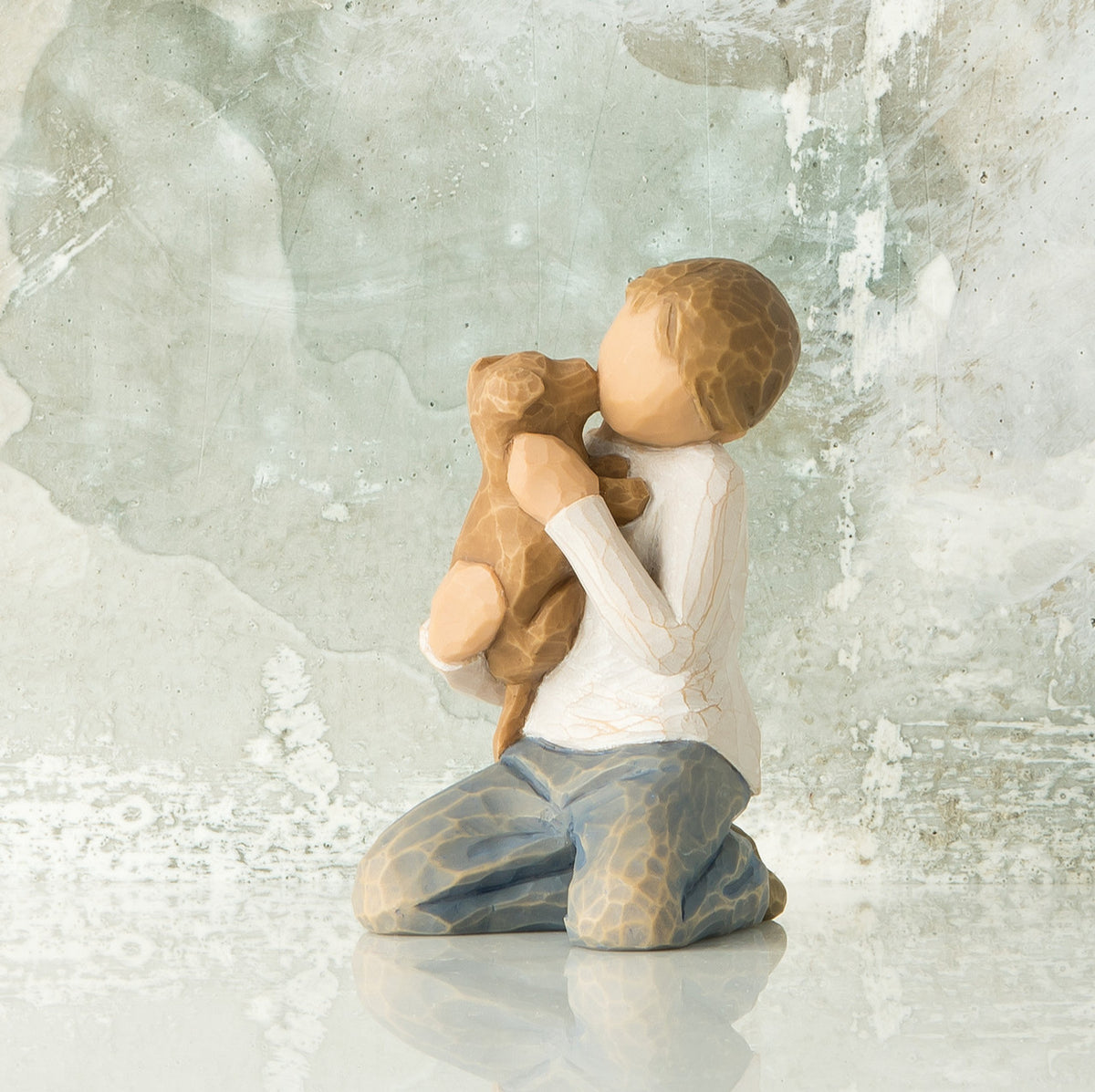 Willow Tree Kindness (boy), 3”h hand-painted resin figure of kneeling boy in neutral clothes, holding golden dog in arms, in front of gray painting