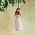 Willow Tree Surrounded by Love Ornament, 4”h hand-painted resin figure in cream dress holding bouquet of poppies to face, brown elastic cord, hanging in front of dark yellow painting