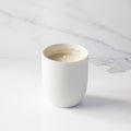 Filled scented candle with unglazed off-white tapered cylinder vessel, sentiment written in gold inside rim, plant-based wax blend, all-cotton wick.