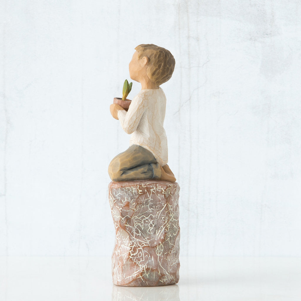 Right side view of boy with brown hair sitting on a stump while holding a small potted plant to his chest
