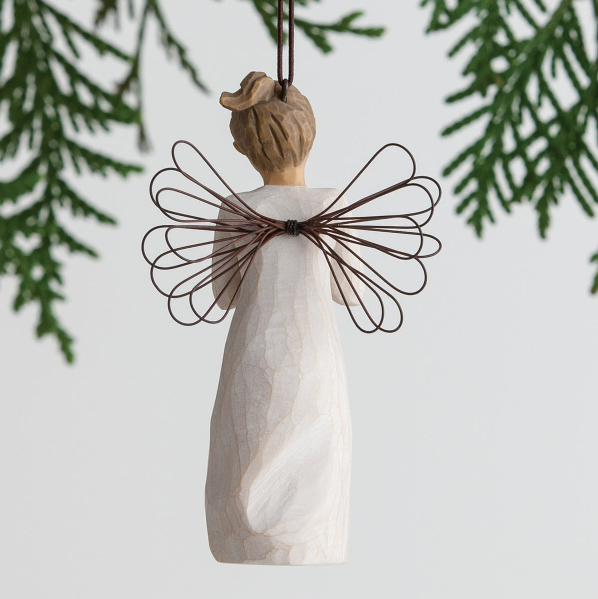 Back view of angel ornament with brown hair in high pony tail leaning forward and holding a red apple up to her face with both hands. Brown string attached to top of angel ornament