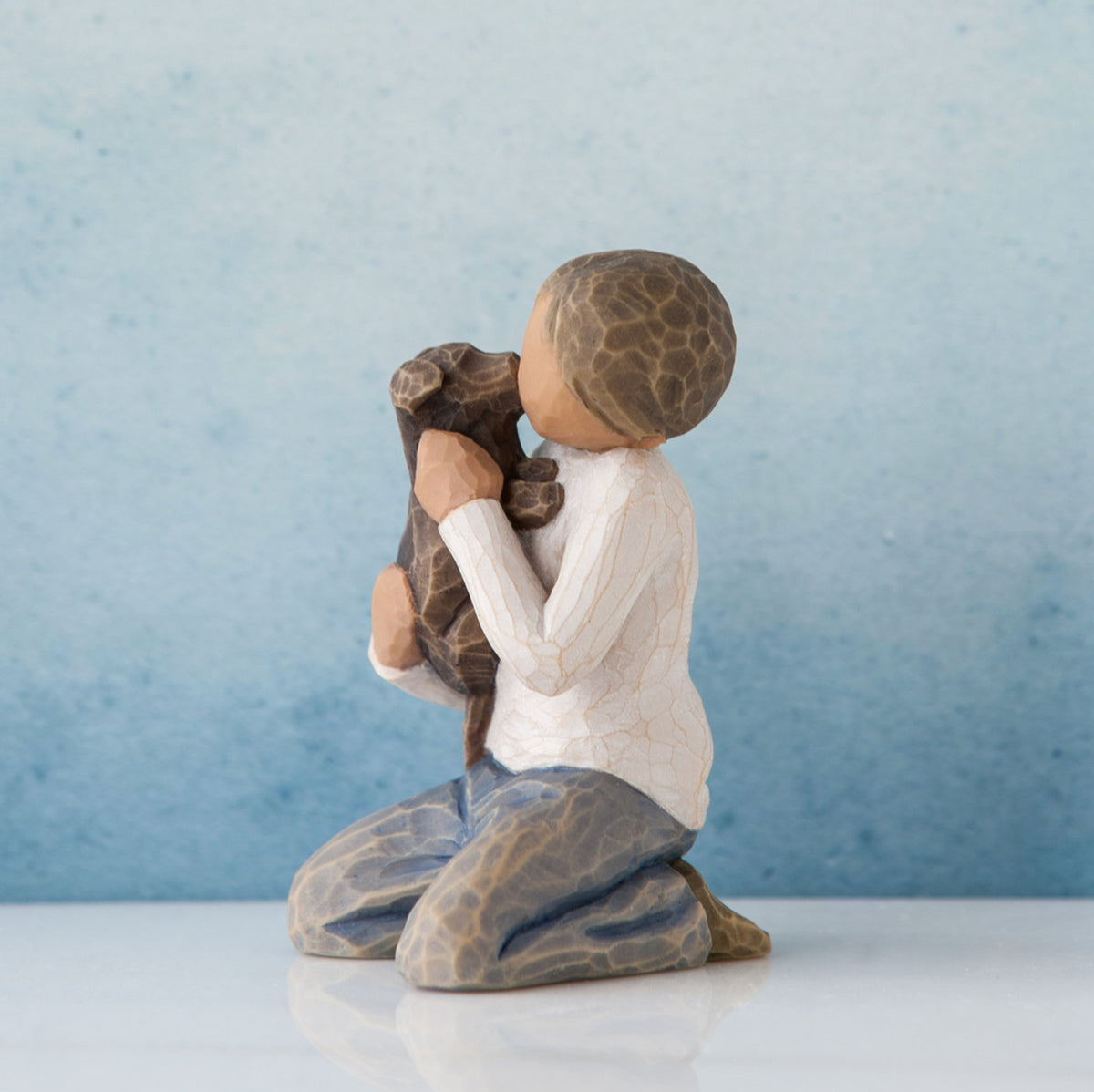 Side view of boy figurine in white shirt and jeans sitting holding brown dog - blue background