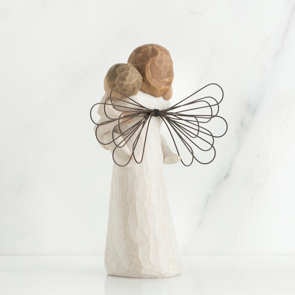 Back view of brunette girl figurine in white dress with brown wings holding baby