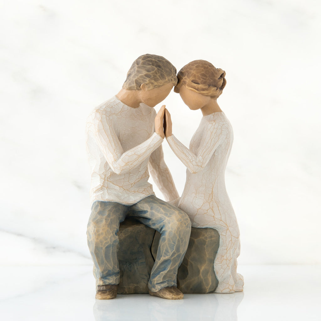 Man and woman figurine sitting on rock dressed in white pressing their hands up against each others