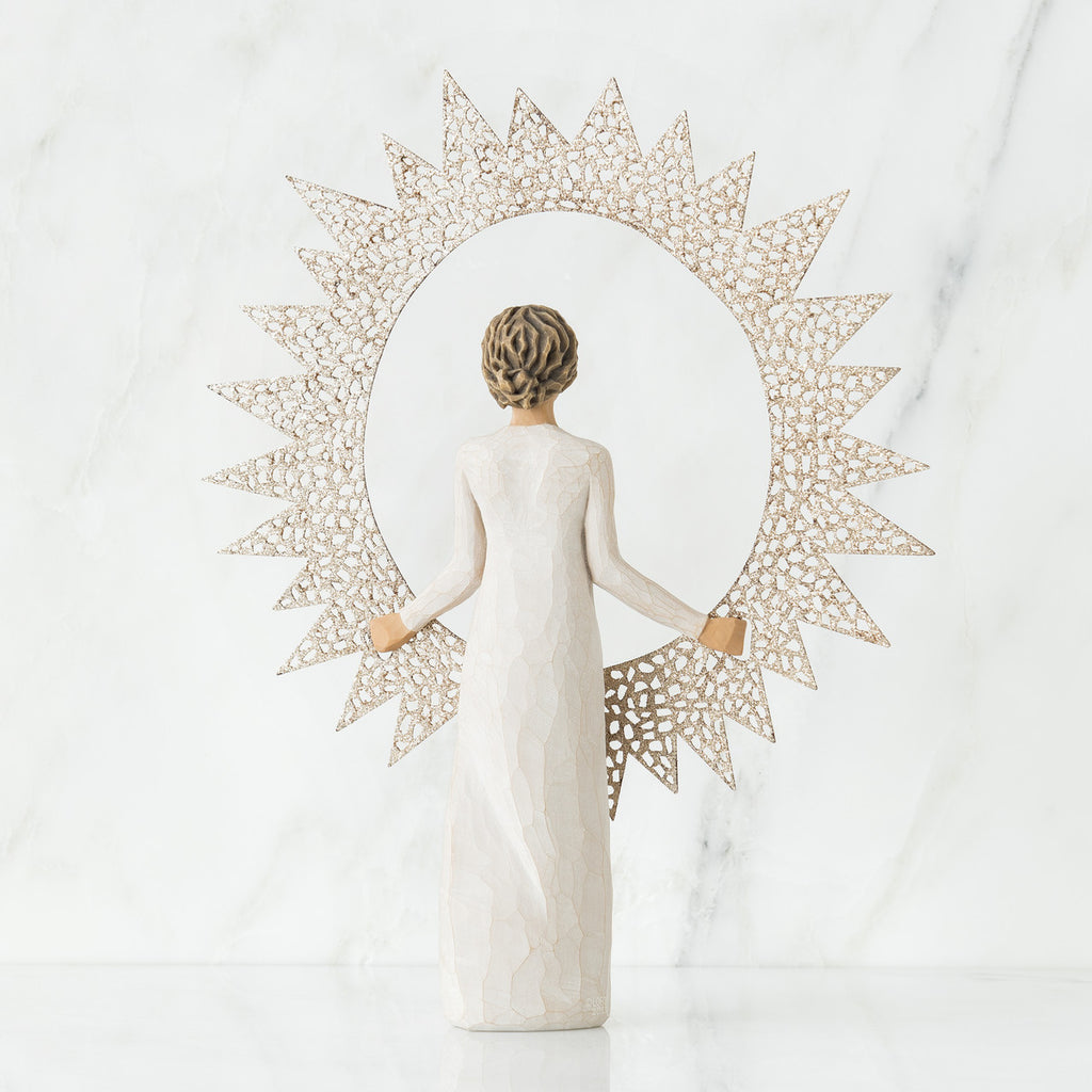 Back view of brunette girl figurine in white dress holding sun figurine up