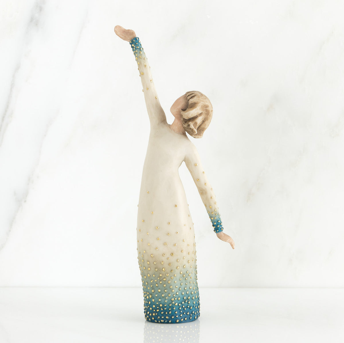 Faceless woman figurine in white dress with blue embellishments - she is facing away from the camera holding both her arms in opposite directions