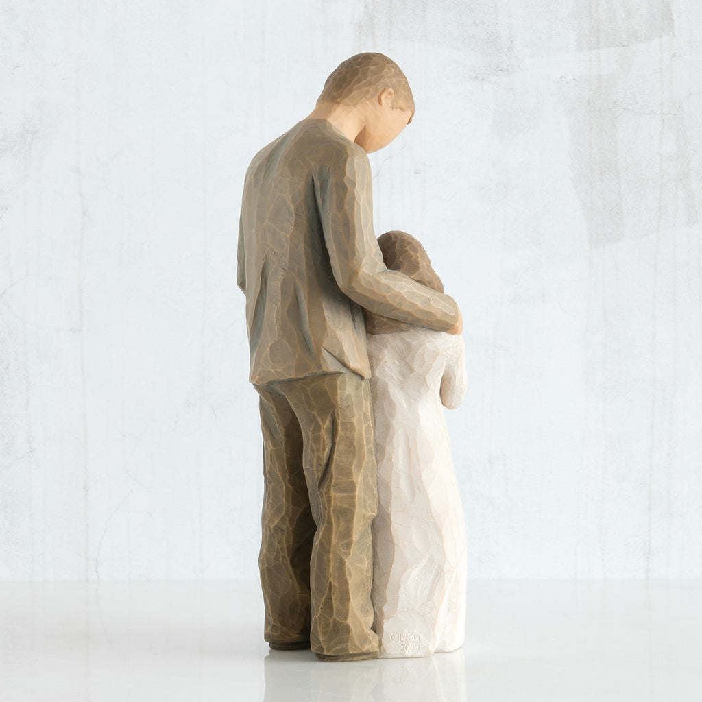 Back view of man figurine in brown looking down at younger daughter in white with arm around her