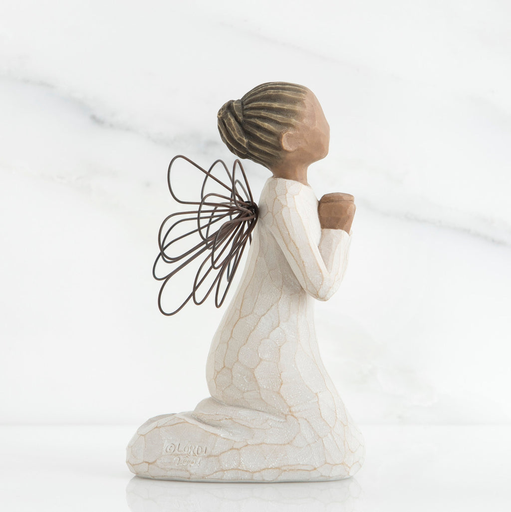 Side view of brunette angel figurine in white dress kneeling holding hands in prayer