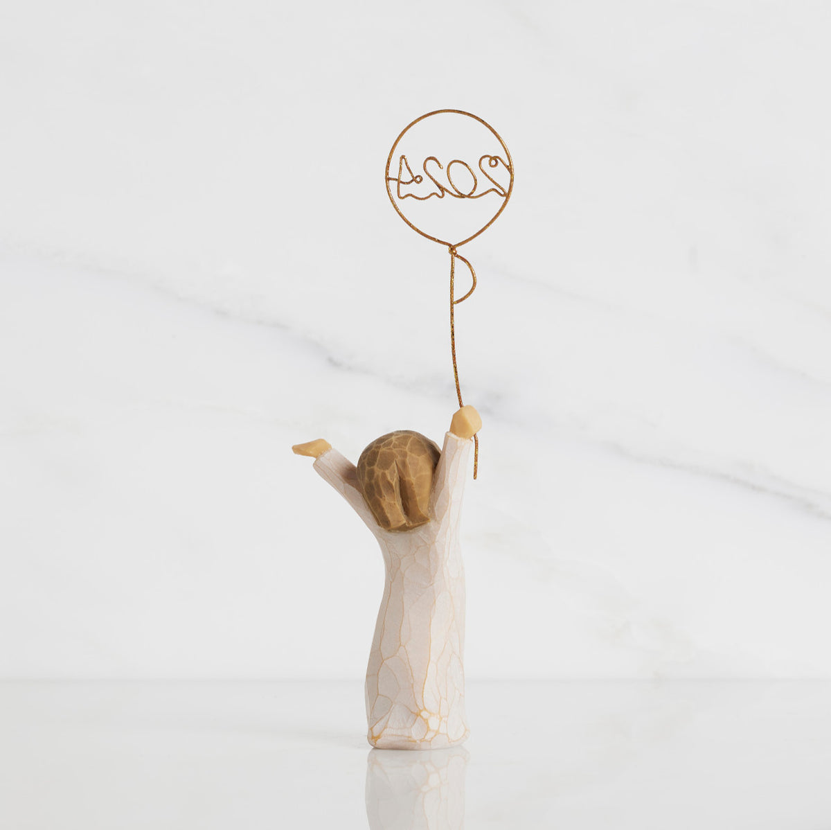 Back view: standing figure in cream dress, arms raised, holding gold wire balloon with 2024 written in gold wire inside