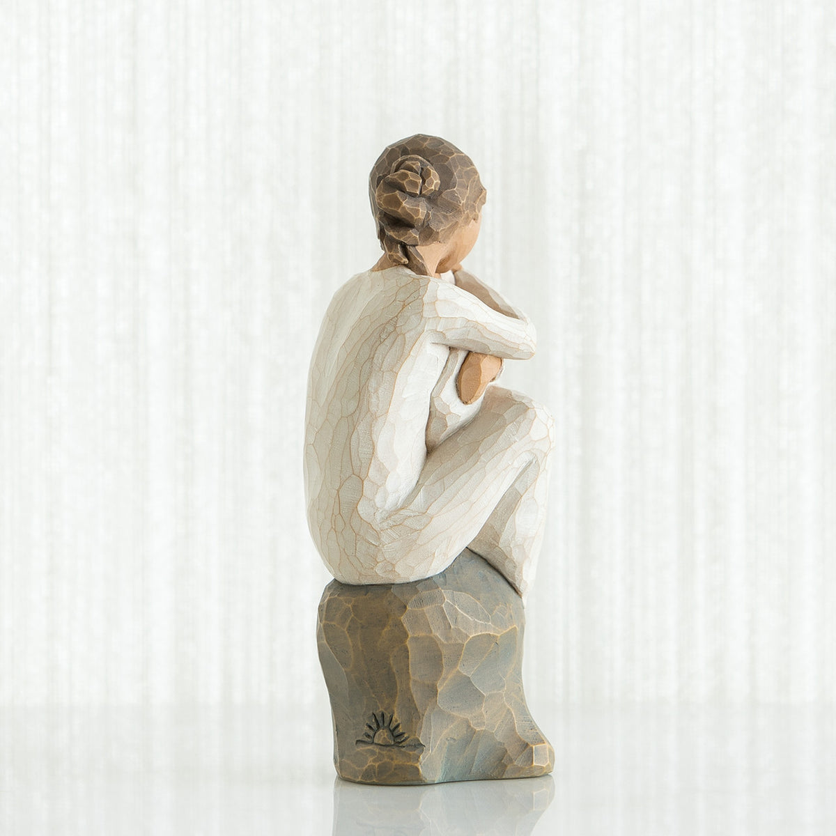 Back view of brunette girl figurine sitting down in white dress on rock