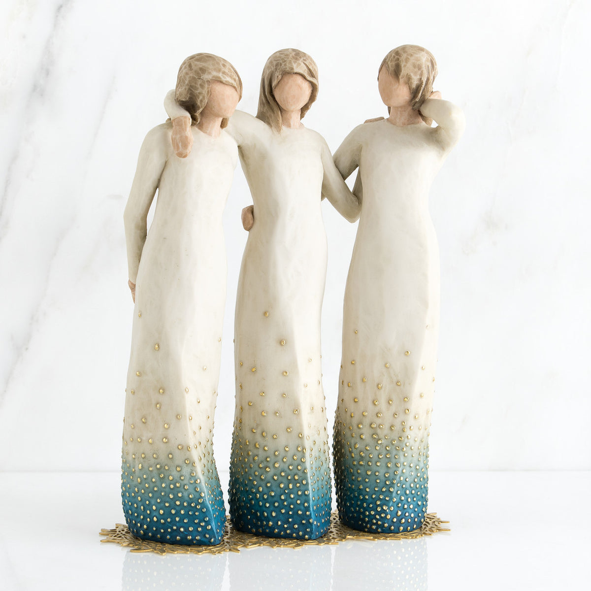 Three brunette woman figurines in white dresses blue bottoms facing forward with arms around each other