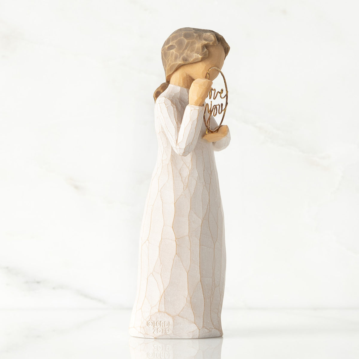 Right-facing view, standing female figure in cream dress, holding gold wire circle in which is written 'love you'