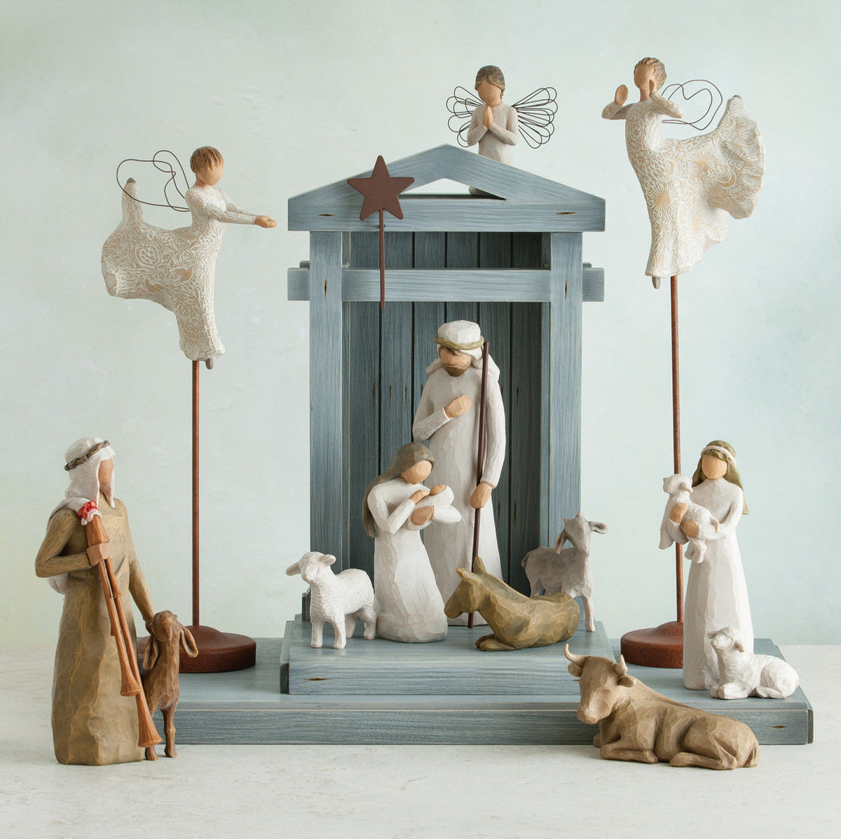 Light grey barn figurine with several wiseman dressed in white, angels, and golden cows laid out